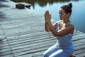 Young woman sitting on a wooden pier with her hands folded in a prayer pose. Meditation, yoga in nature Royalty Free Stock Photo