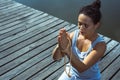 Young woman sitting on a wooden pier with her hands folded with a rosary in a prayer pose. Meditation, yoga in nature Royalty Free Stock Photo