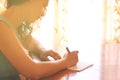 Young woman sitting and writing letter near bright window light. filtered image. Royalty Free Stock Photo