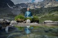 Young woman is sitting in yoga lotus position against the turquoise lake in the mountains Royalty Free Stock Photo