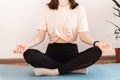 Young woman sitting on a yoga mat and practicing meditation. Relaxation, rest, mental health. Exercises at home in the room Royalty Free Stock Photo