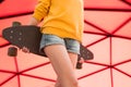 Young woman with skateboard against vivid red wall