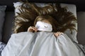 Young woman is sleeping in bed with sleep mask and peeking from underneath the sleeping mask