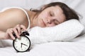 Young woman is sleeping in bed and turns off alarm. Sleep after alarm clock rang. girl wakes up on alarm clock in early morning. Royalty Free Stock Photo