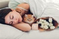 Young woman sleeping near bouquet of roses and gift box in bed with cat. Present left by boyfriend for Women`s day Royalty Free Stock Photo