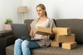 Young woman small online business owner sitting on couch and preparing package for shipping on laptop at home Royalty Free Stock Photo