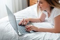 Young woman smile typing on laptop keyboard while lying in bed at home. Happy teen girl communicates online working remote, Royalty Free Stock Photo