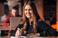 Young woman smiling at camera while working remotely in coffee shop. Positive female with notepad Royalty Free Stock Photo