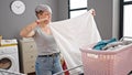 Young woman smiling confident folding towel at laundry room