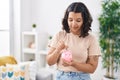 Young woman smiling confident inserting coin on piggy bank at home Royalty Free Stock Photo