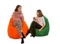 Young woman and smiling girl sitting on beanbag chairs and drink