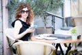 Young woman smiling in pleasure as she reads a message on her mobile phone while Sitting outdoors on the seat of a restaurant. Royalty Free Stock Photo