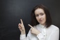 Young woman is smiling and pointing up, against black chalkboard Royalty Free Stock Photo