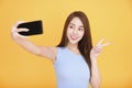 young woman smiling and taking self photo smartphone isolated over yellow background