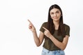Young woman smirk and look up thoughtful, pointing fingers left at something boring or disappointing, standing skeptical Royalty Free Stock Photo