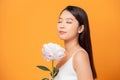 Young woman sniffing pink peony flower closed her eyes on yellow background