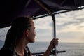 Young woman, solo traveler on boat at sea admires sunset