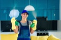 Young woman in special cleaning clothes holds two bottles of different detergents, standing on the hi-tech kitchen