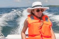 Young woman on a speed boat in a life jacket on a background foamy trace of the boat.