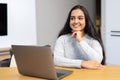 Young woman spending home leisure with laptop. Calm girl sitting at the table and looking away in front of the laptop