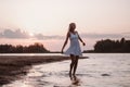 A young woman is spinning on the beach. A beautiful slender happy blonde in a white summer dress dances on the river Royalty Free Stock Photo