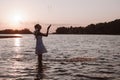 A young woman splashes water. Photo of a slender, beautiful, happy blonde in a summer dress and a straw hat standing in