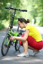 Young woman in sport clothes repairs bike in park Royalty Free Stock Photo