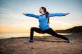 Young woman in sports clothes doing yoga on the beach. Sunset and ocean in the background. Wellness and sports lifestyle Royalty Free Stock Photo