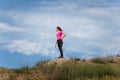 Young woman in sportswear standing on hill top on blue sky background. Fitness, healthy way of life, wellbeing, freedom Royalty Free Stock Photo