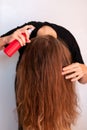 Young woman spraying her wavy blond long hair for sun and heat protection. Treatment
