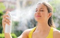 Young woman spraying Thermal Water on her face outside. Thermal water used for skin care, fix makeup, help skin irritation,