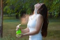 Young woman spraying water on herself from a spray bottle in a summer park Royalty Free Stock Photo