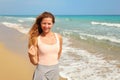 Young woman squinting one eye, as strong sun shines on her at the beach, sea in background