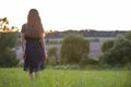 Young woman standing alone on a field with green grass enjoying warm sunset Royalty Free Stock Photo