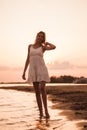 A young woman is standing on the beach. A beautiful slender happy blonde is smiling and posing against the sunset in a Royalty Free Stock Photo