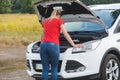 Young woman standing at broken car and looking under the hood Royalty Free Stock Photo