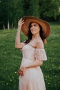 Young woman standing on a countryside background, outdoors, laughing, wearing a vintage dress and a straw hat Royalty Free Stock Photo