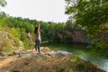 Young woman standing on edge of rock and stretching, practicing yoga. view of quarry with water.