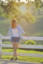 Young woman is standing by a fence on a ranch in warm toned