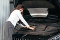 Young woman standing in front of the car with opened hood in garage looking under car hood Royalty Free Stock Photo