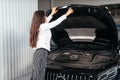 Young woman with opened hood in garage looking under car hood Royalty Free Stock Photo