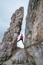 Young woman standing high between two tall, vertical rocks, at the beginning of the via ferrata route towards Averau peak