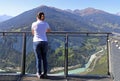 A young woman is standing high up on a viewpoint in the mountains