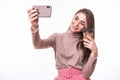 Young woman standing holding takeaway coffee in hand and taking selfie on mobile phone isolated over white background Royalty Free Stock Photo