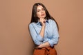 Freestyle. Young girl standing studio isolated on brown touching chin posing to camera pensive Royalty Free Stock Photo