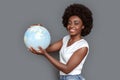 Young woman standing on gray with globe looking camera joyful traveling around world