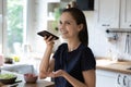 Young woman standing in kitchen holds smartphone talks on speakerphone