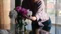 A young woman standing in a modern cozy living room puts a vase with a bouquet of beautiful fresh lilac peonies on the Royalty Free Stock Photo