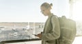 Young woman standing near airport gates window holding cellphone in her hands, wearing travel backpack and walking to Royalty Free Stock Photo