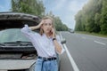 Young woman standing near broken down car with popped up hood having trouble with her vehicle. Waiting for help tow truck or Royalty Free Stock Photo